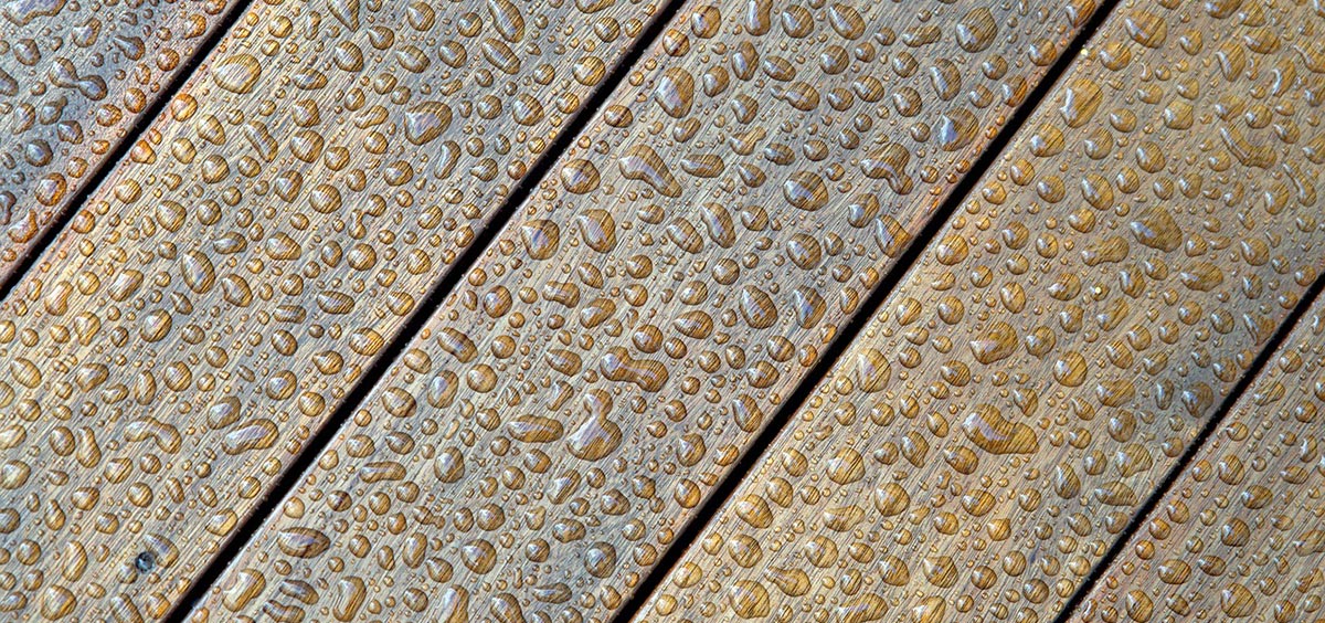 Gros plan sur des lames de terrasse en bois avec gouttes d’eau, illustrant l’importance du traitement et de la protection dans un plan de terrasse bien conçu.