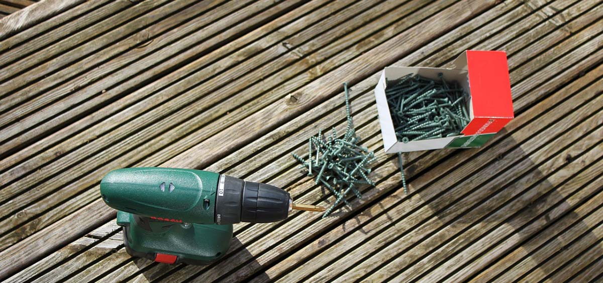 Perceuse et visserie utilisées pour l’installation d’une terrasse en bois, posées sur les lames.