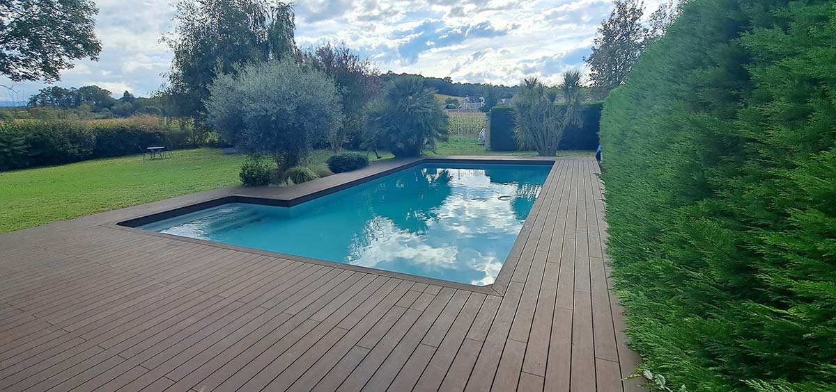 Terrasse en bambou entourant une piscine extérieure, intégrée dans un jardin paysager avec végétation dense.