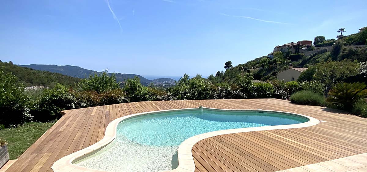 Terrasse en bois exotique entourant une piscine extérieure, avec vue panoramique sur la végétation et les collines 