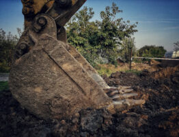 Godet d’excavatrice creusant la terre pour le décaissement d’une future terrasse en bois, sur chantier extérieur.
