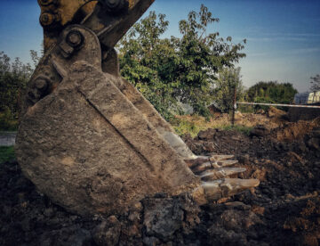 Godet d’excavatrice creusant la terre pour le décaissement d’une future terrasse en bois, sur chantier extérieur.