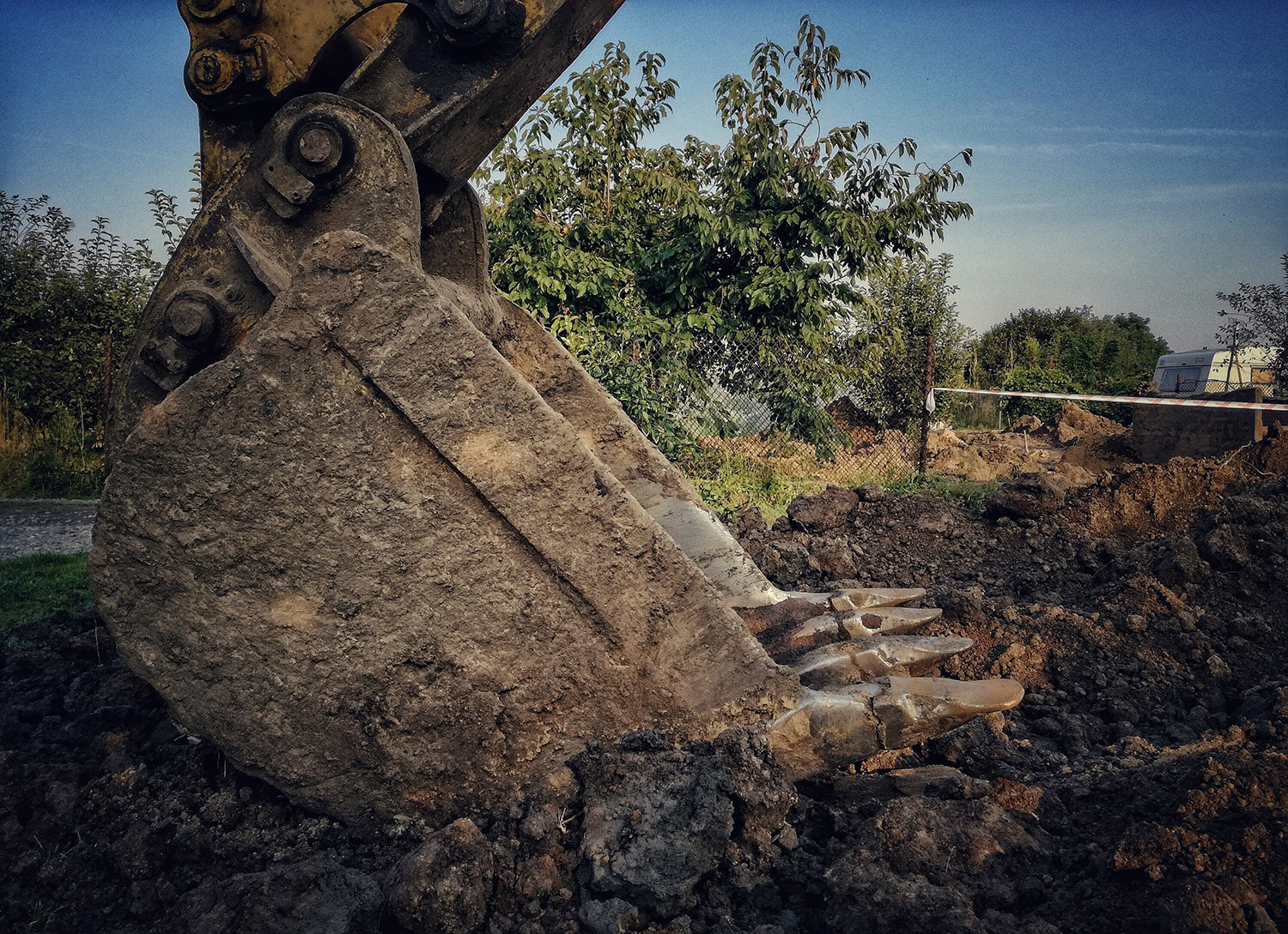 Godet d’excavatrice creusant la terre pour le décaissement d’une future terrasse en bois, sur chantier extérieur.