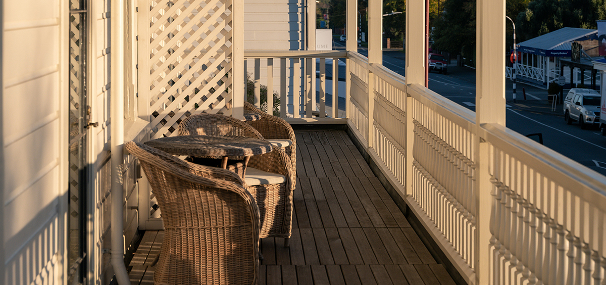 Terrasse en bois clair avec garde‑corps blanc et mobilier en rotin, baignée de lumière naturelle.