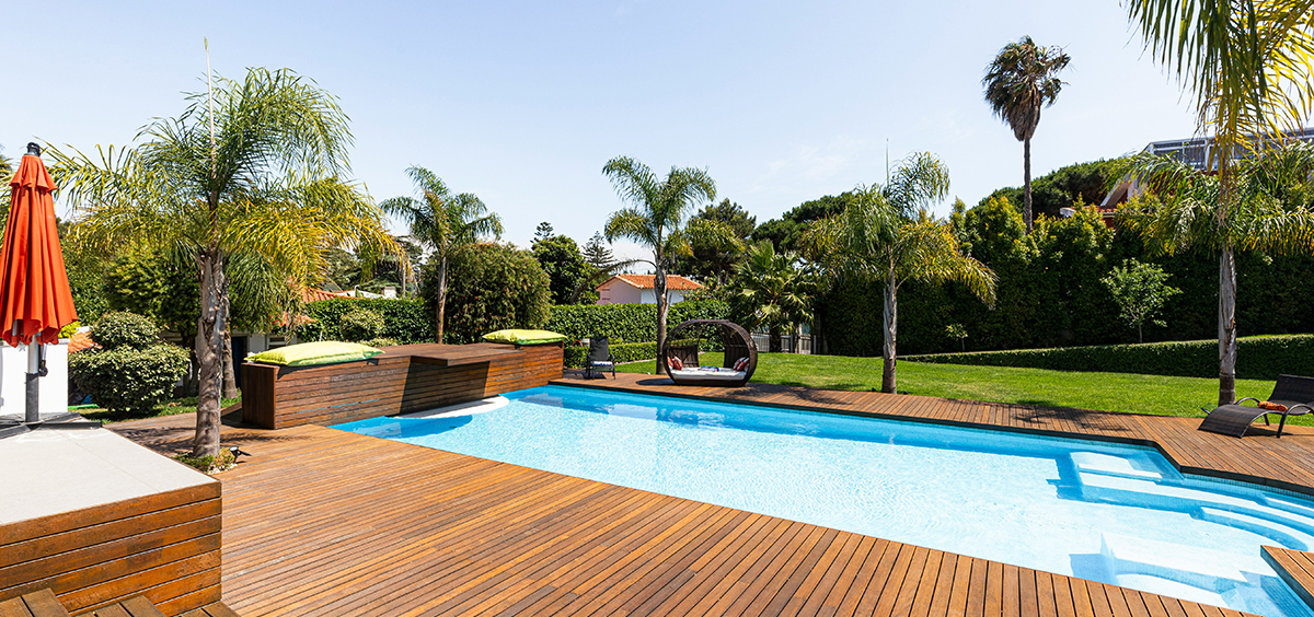 Terrasse bois exotique autour d’une piscine, avec palmiers et mobilier design, illustrant la noblesse et la valeur patrimoniale du matériau.